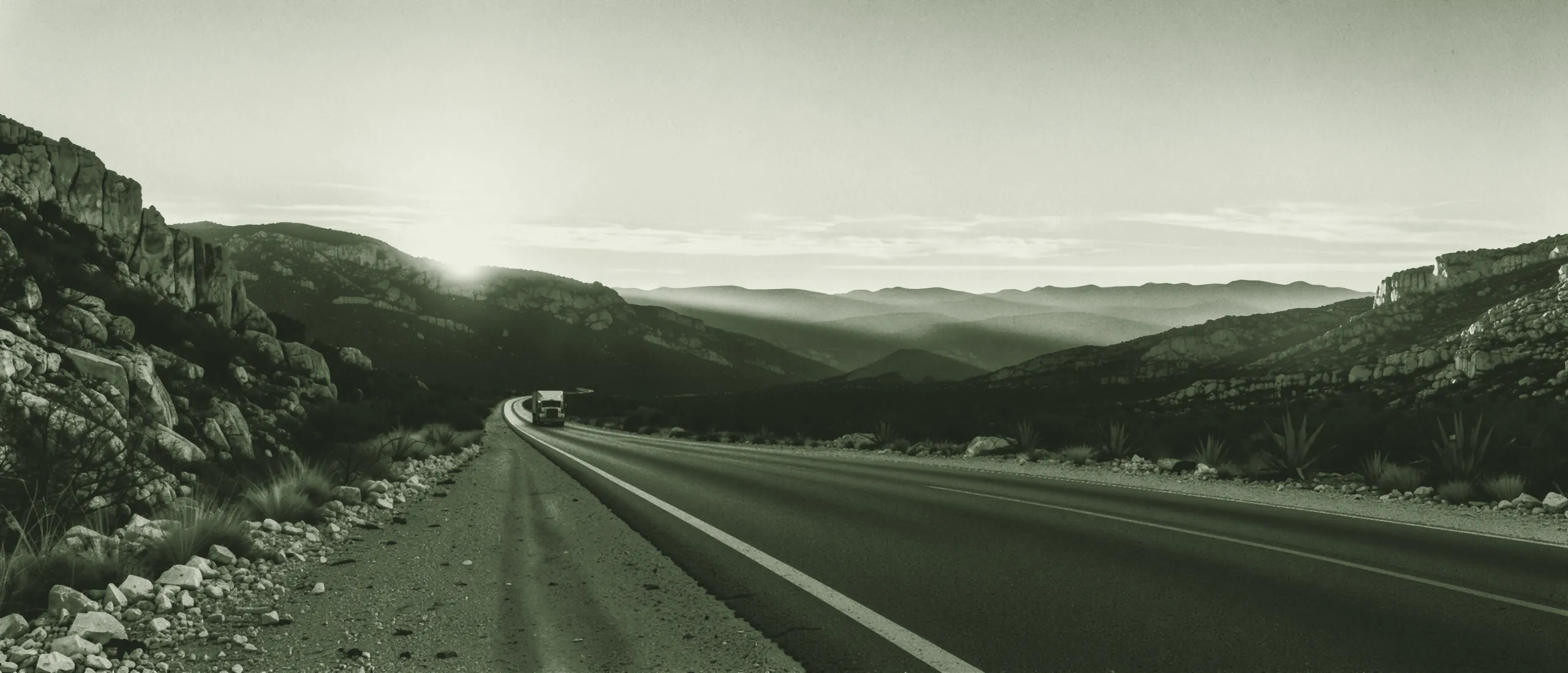 Carretera entre montañas de piedra caliza al amanecer, con un tractocamión a lo lejos